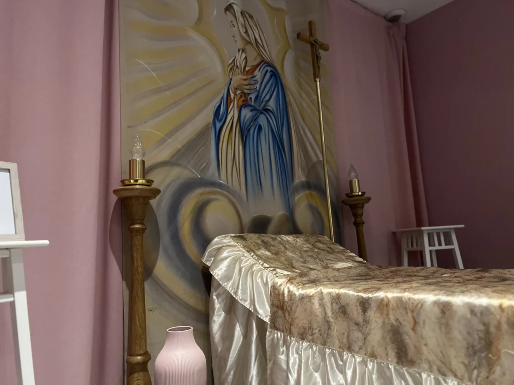 Décor d'un salon funéraire avec fresque religieuse et chandeliers dorés.
