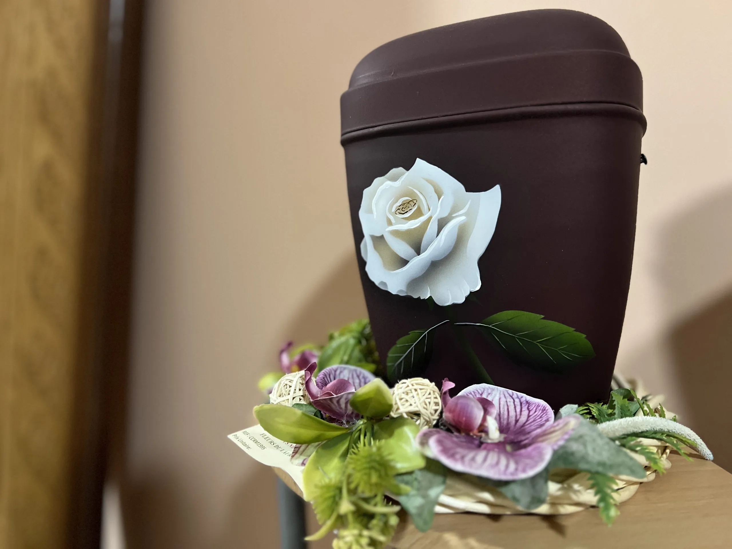 Urne funéraire brune décorée d'une rose blanche et entourée d'orchidées.
