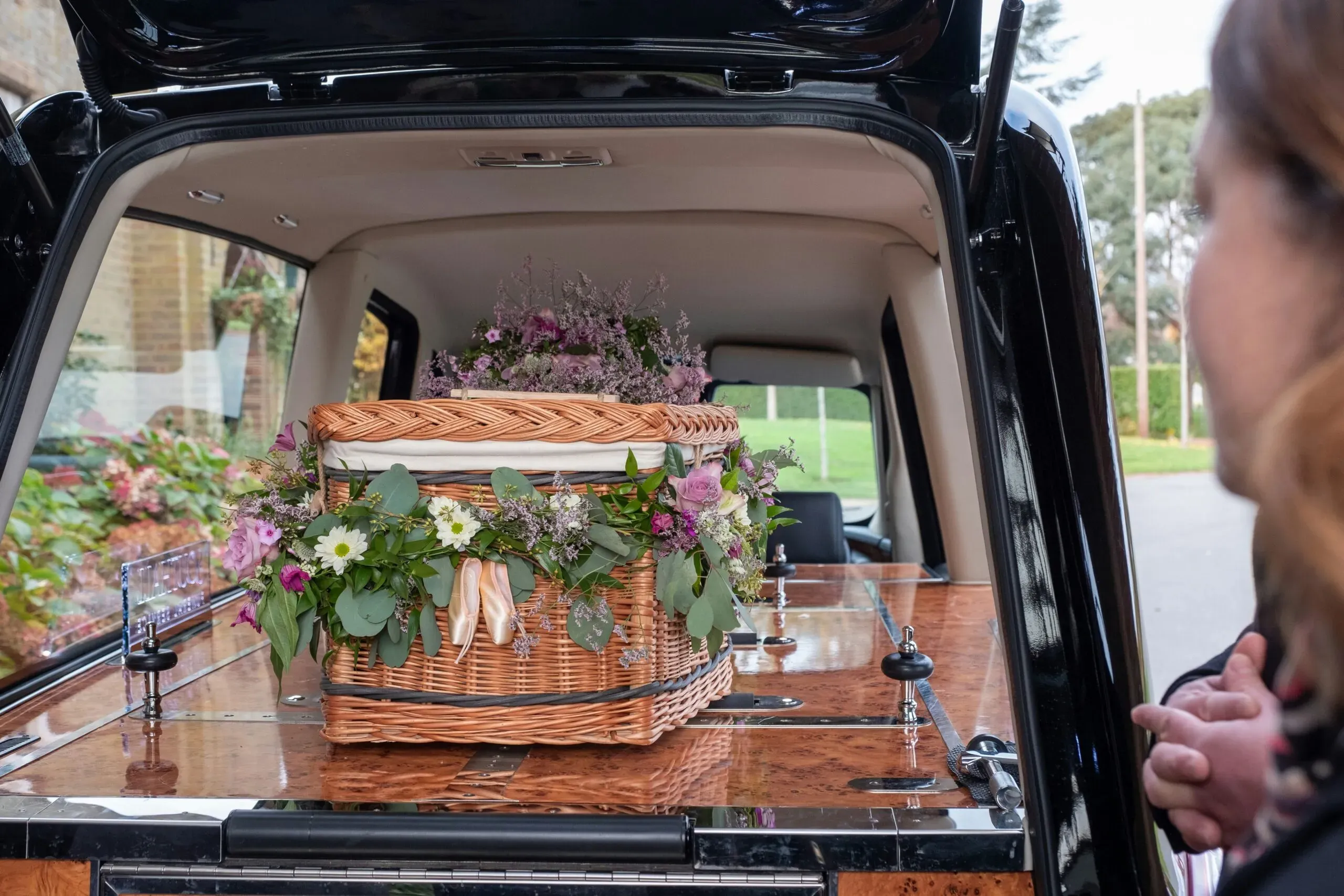 Cercueil en osier tressé orné de fleurs dans le coffre d'un corbillard.