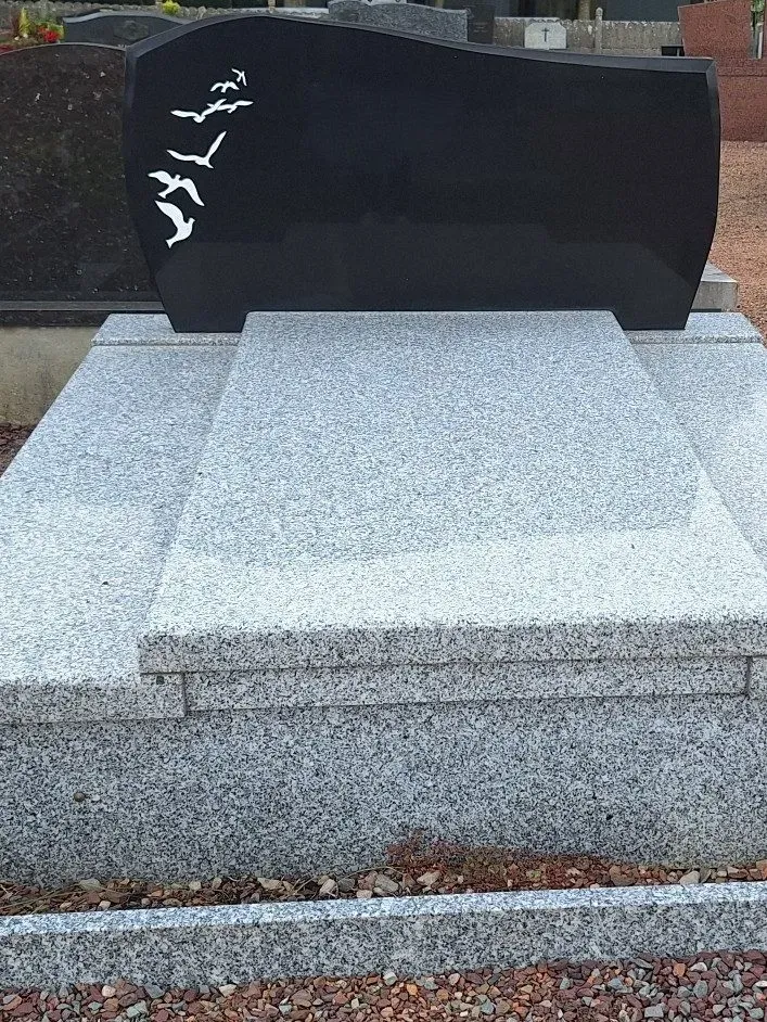 Monument funéraire bicolore poli dans un cimetière paysager.