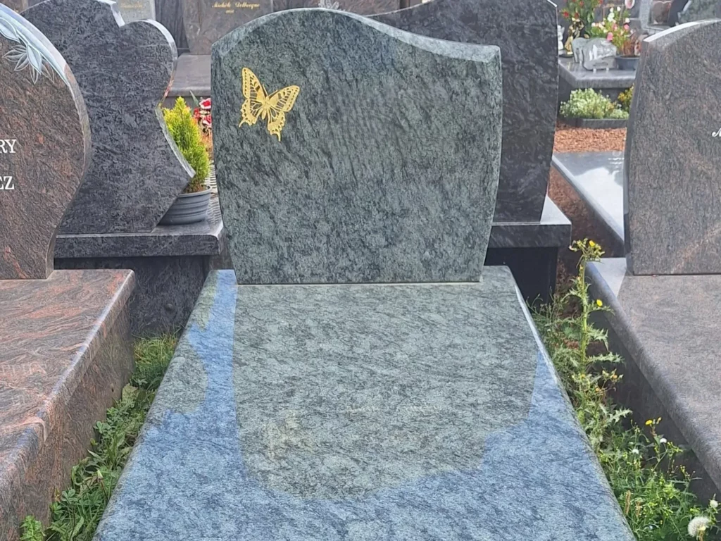 Tombe en granit veiné vert et gris ornée d'un papillon doré gravé.