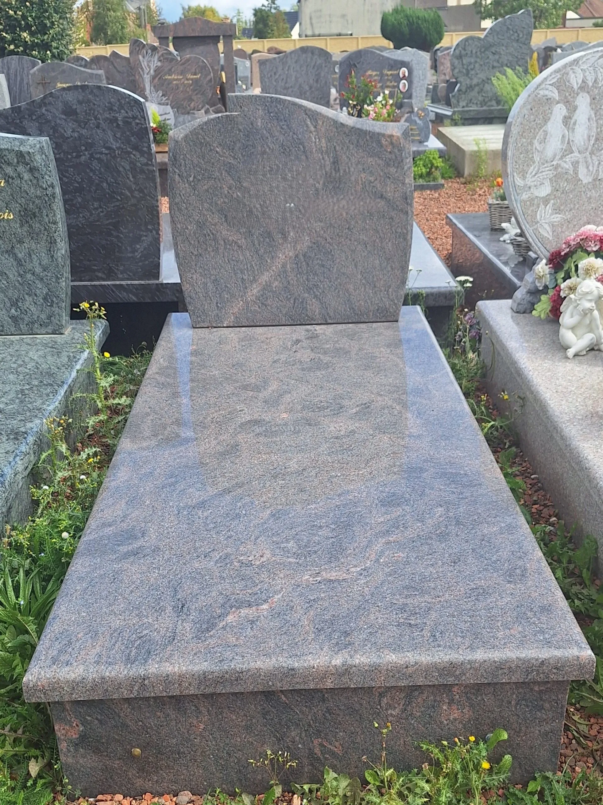Monument funéraire bicolore en granit avec stèle tombale de forme cintrée.