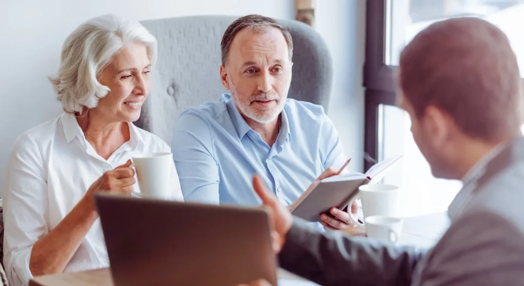 Couple de seniors en entretien avec un conseiller en prévoyance autour d'un ordinateur.