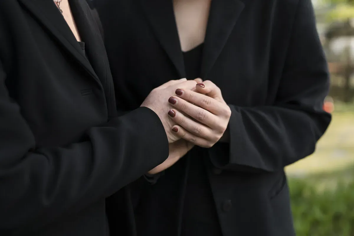 Deux personnes en tenue sombre se tenant la main lors de funérailles.